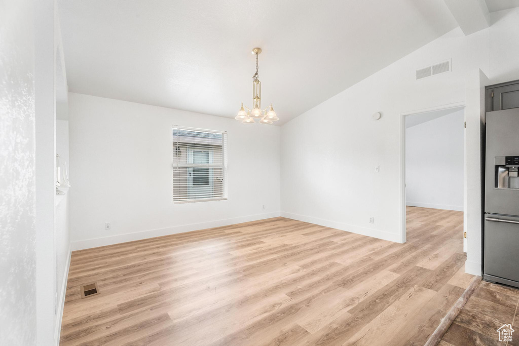 Unfurnished room with lofted ceiling, a chandelier, light wood-type flooring, and baseboards