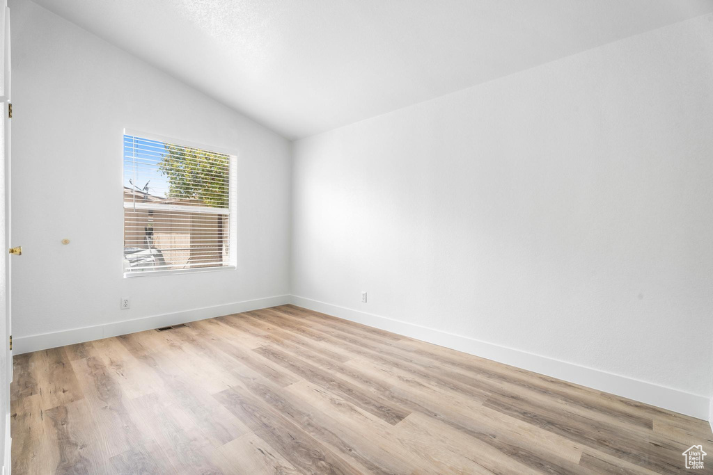 Unfurnished room with vaulted ceiling, light wood-type flooring, and baseboards