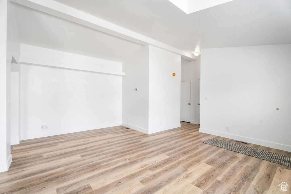 Spare room featuring light wood finished floors, baseboards, and a skylight