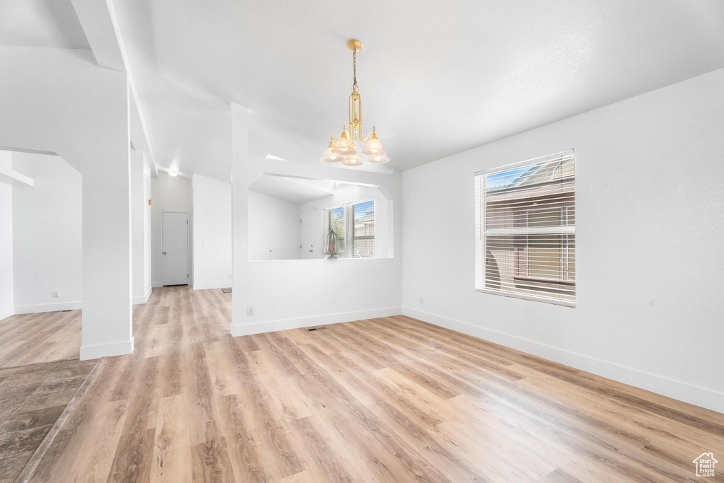 Unfurnished living room featuring light wood-style flooring, a chandelier, baseboards, and lofted ceiling