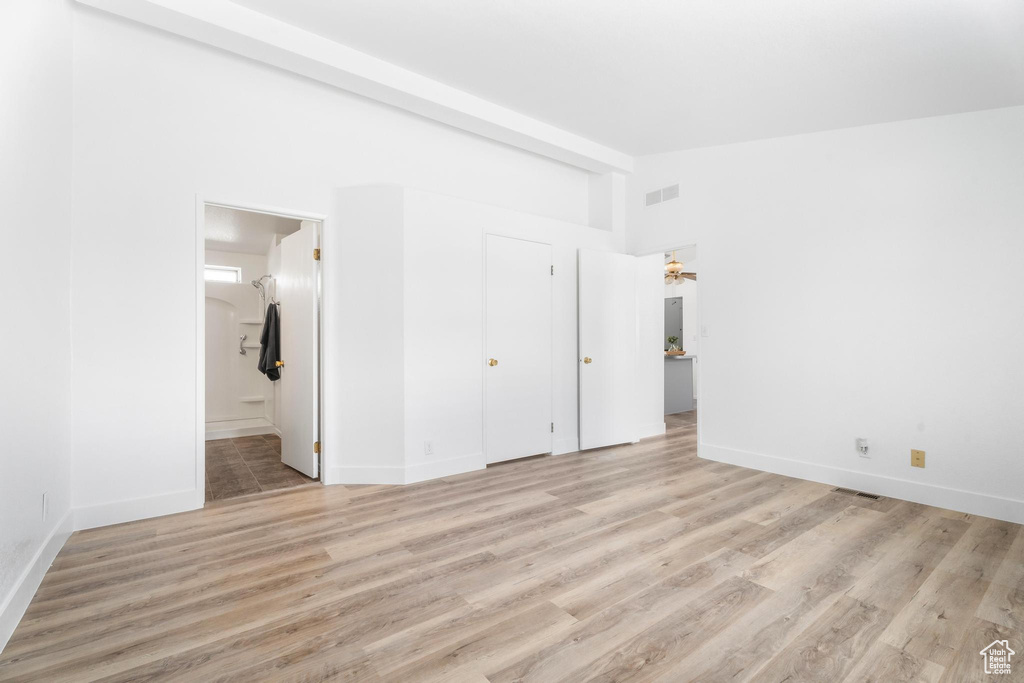 Unfurnished bedroom featuring lofted ceiling, light wood-type flooring, baseboards, and ensuite bath