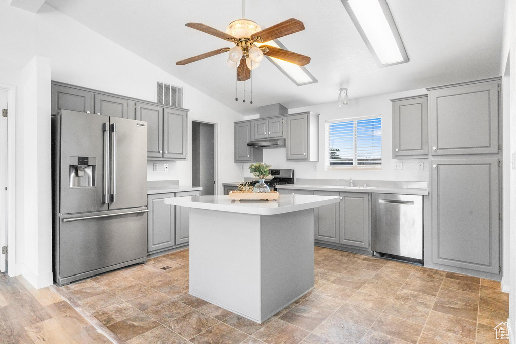 Kitchen with appliances with stainless steel finishes, gray cabinetry, under cabinet range hood, light countertops, and lofted ceiling