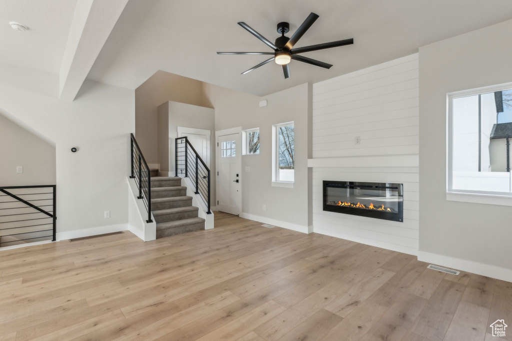 Unfurnished living room featuring healthy amount of natural light, ceiling fan, baseboards, and lofted ceiling