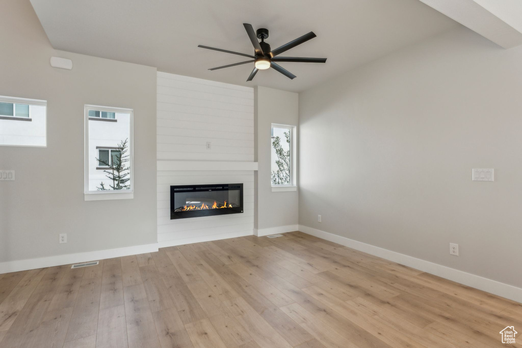 Unfurnished living room with a large fireplace, ceiling fan, light wood-style flooring, and baseboards