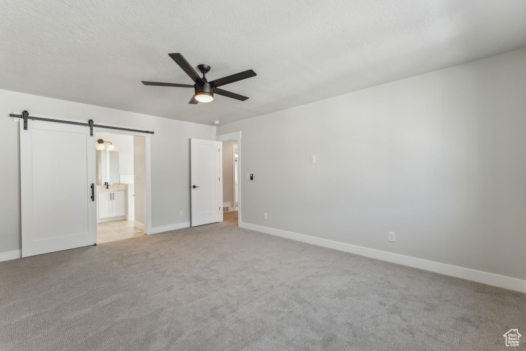 Unfurnished bedroom featuring a barn door, baseboards, light carpet, ensuite bathroom, and ceiling fan