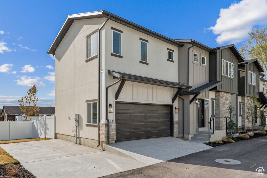 View of front of house featuring fence, stone siding, a garage, concrete driveway, and board and batten siding