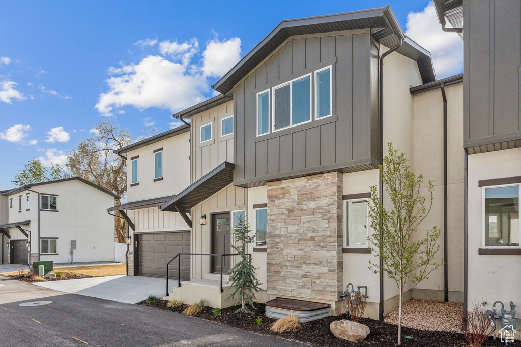 Contemporary house featuring board and batten siding, stone siding, an attached garage, concrete driveway, and cooling unit