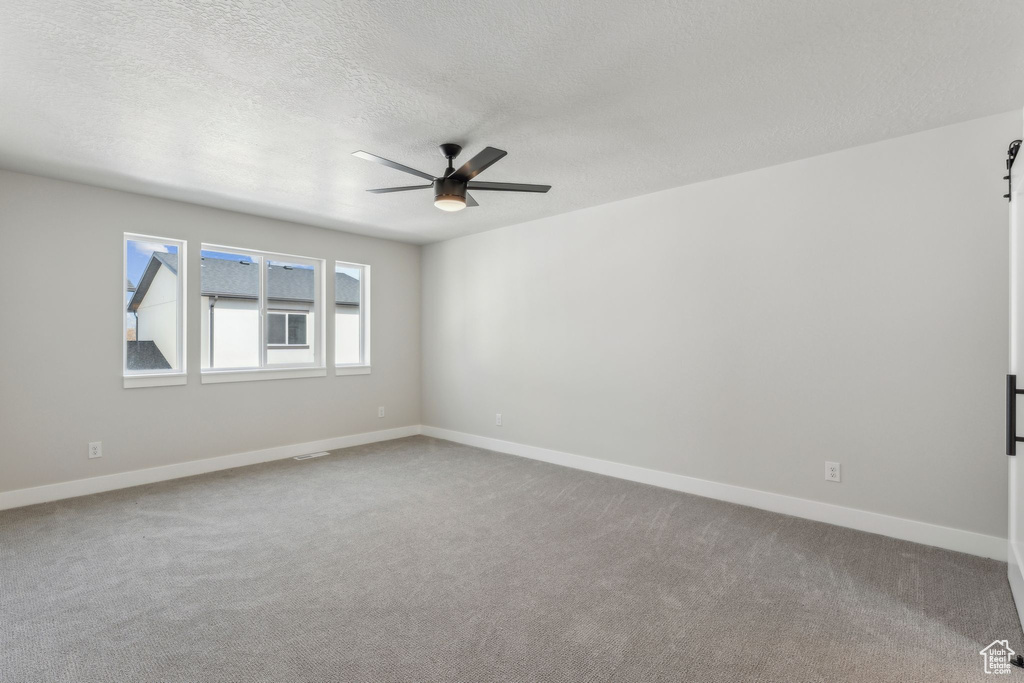 Carpeted empty room with a ceiling fan, a textured ceiling, and baseboards