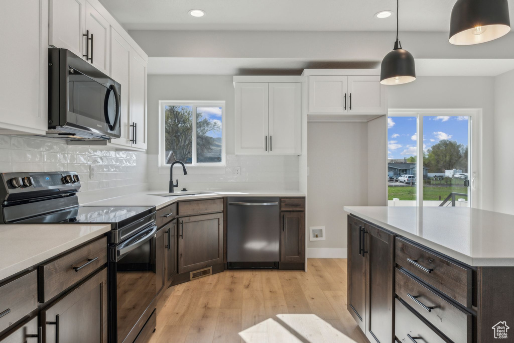 Kitchen featuring stainless steel dishwasher, black range with electric cooktop, a sink, light wood-style floors, and white cabinets