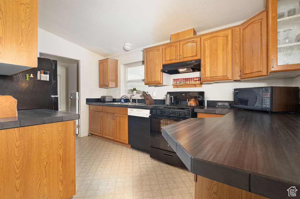 Kitchen featuring black appliances, under cabinet range hood, dark countertops, vaulted ceiling, and light floors