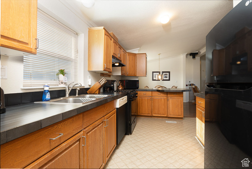 Kitchen with a sink, dark countertops, a peninsula, and under cabinet range hood