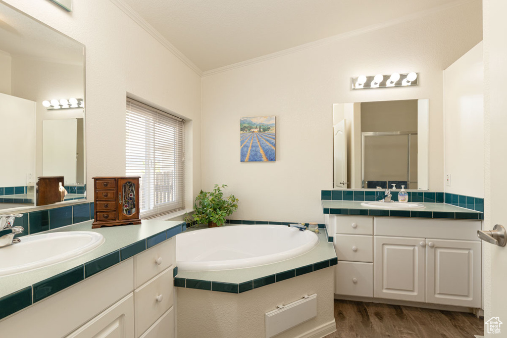 Full bath featuring crown molding, a stall shower, two vanities, wood finished floors, and a garden tub