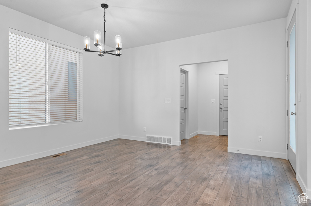 Empty room featuring a chandelier, wood-type flooring, baseboards, and healthy amount of natural light