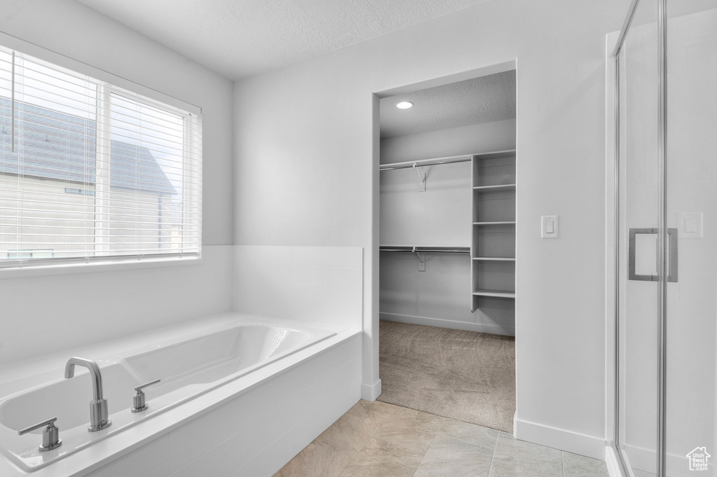 Bathroom with a textured ceiling, a shower stall, a walk in closet, a garden tub, and baseboards
