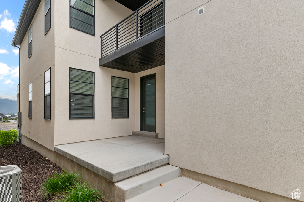 Entrance to property featuring stucco siding, a balcony, a patio area, and central AC unit