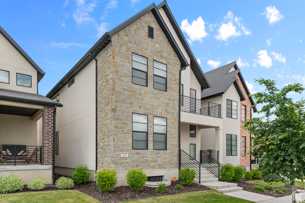 View of front of house featuring stone siding, a balcony, and stucco siding