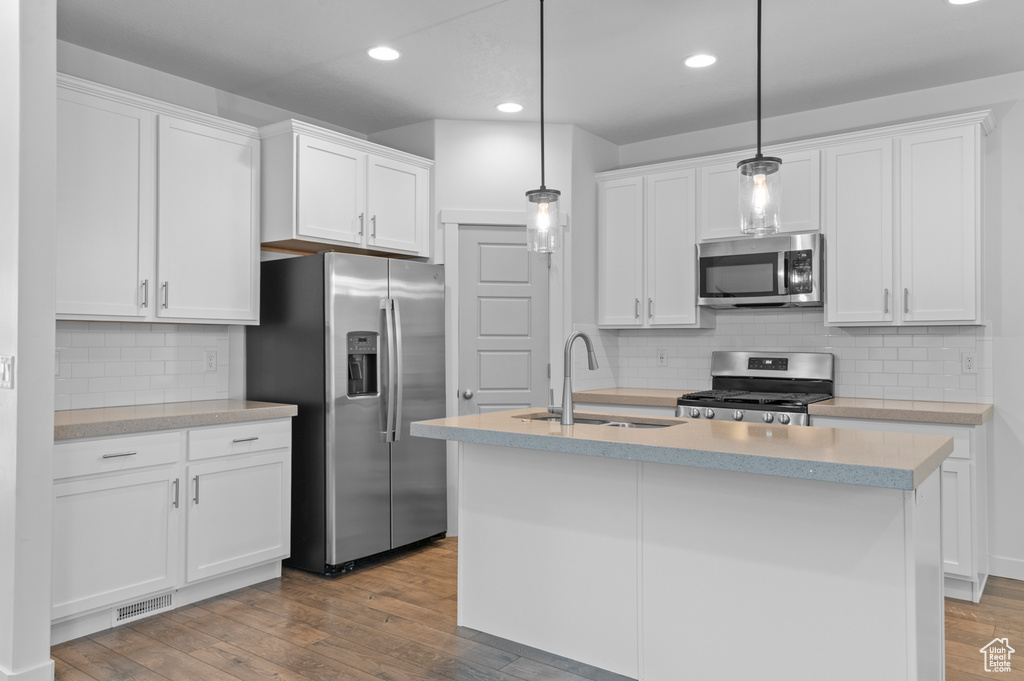 Kitchen featuring stainless steel appliances, a sink, white cabinets, wood finished floors, and recessed lighting