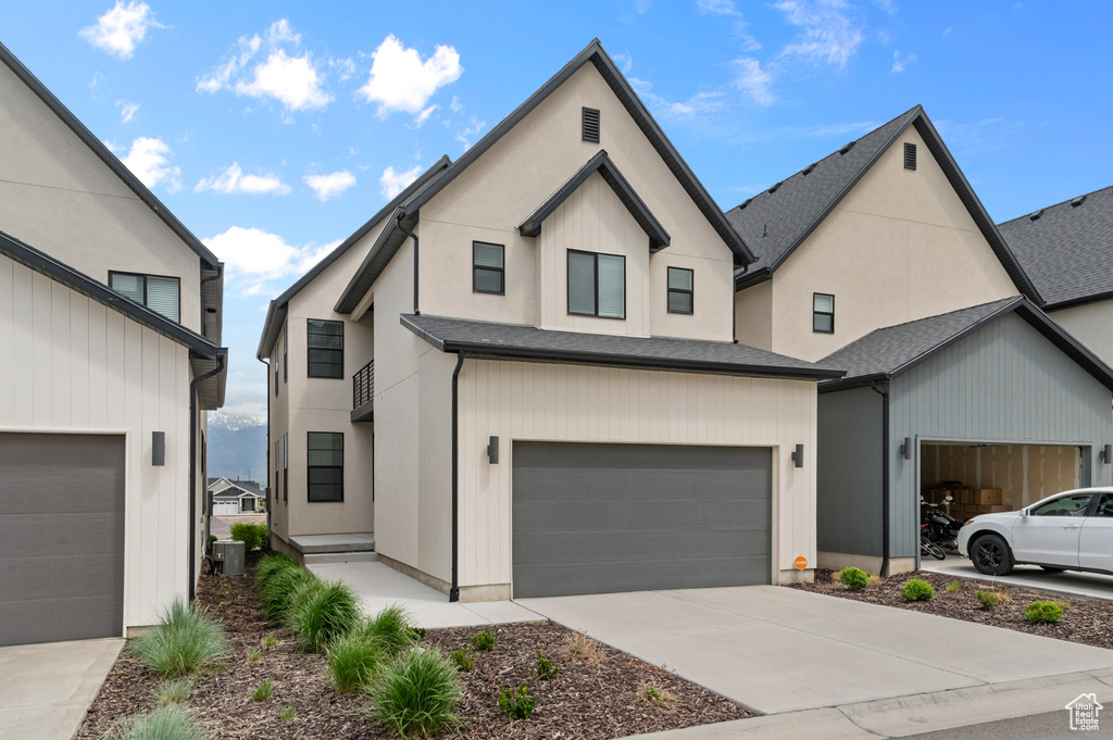 View of front facade featuring cooling unit, concrete driveway, a garage, and a shingled roof