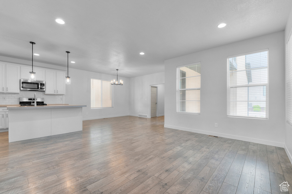 Kitchen featuring appliances with stainless steel finishes, open floor plan, a chandelier, recessed lighting, and white cabinetry