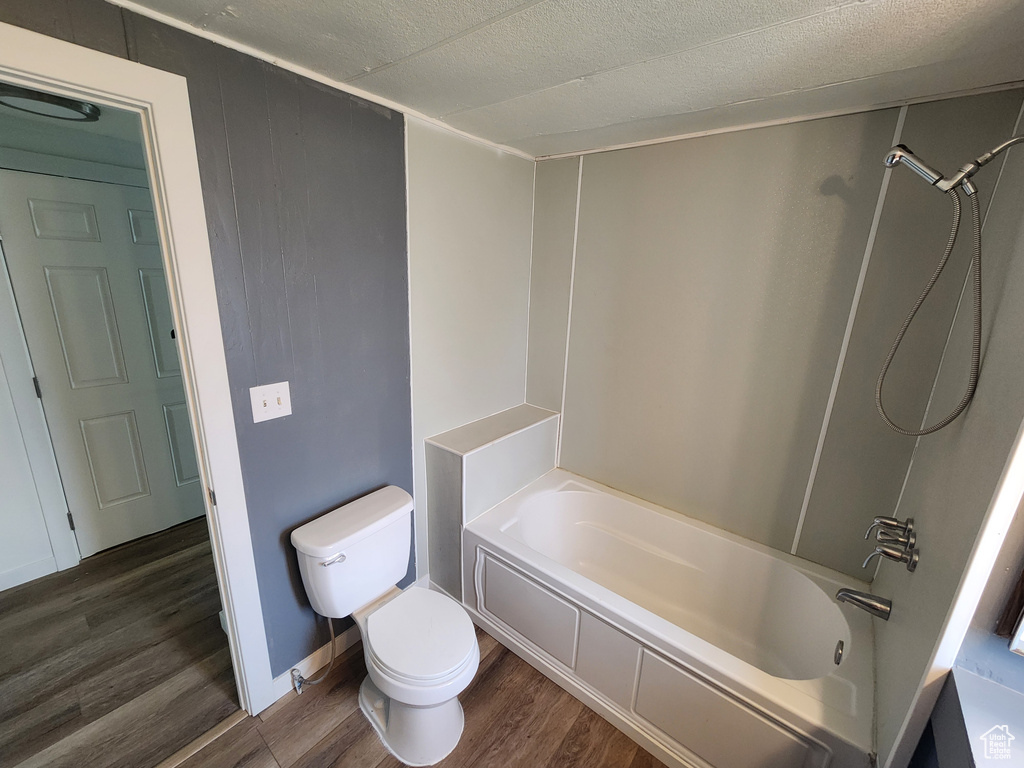 Bathroom featuring wood finished floors, toilet,  shower combination, and a textured ceiling