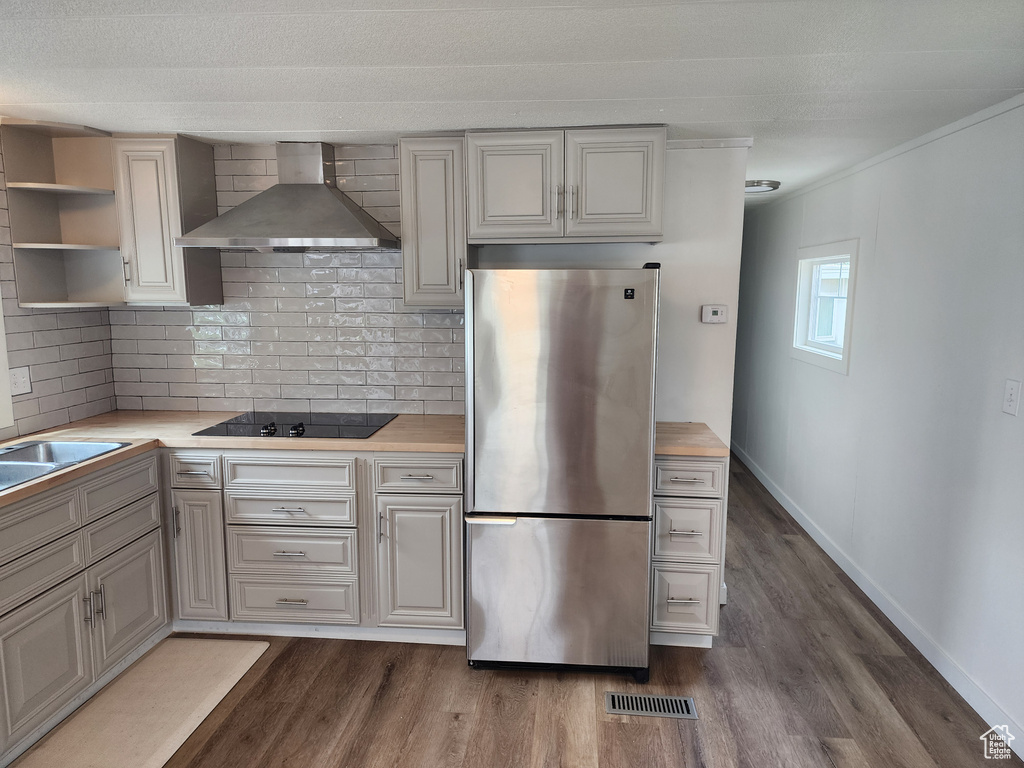 Kitchen featuring freestanding refrigerator, wall chimney exhaust hood, black electric stovetop, and dark wood-style flooring
