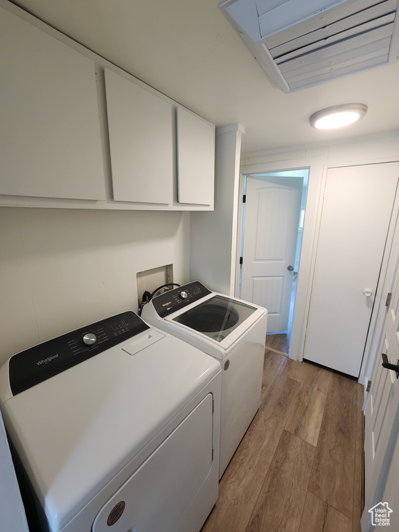 Laundry area with cabinet space, separate washer and dryer, and wood finished floors