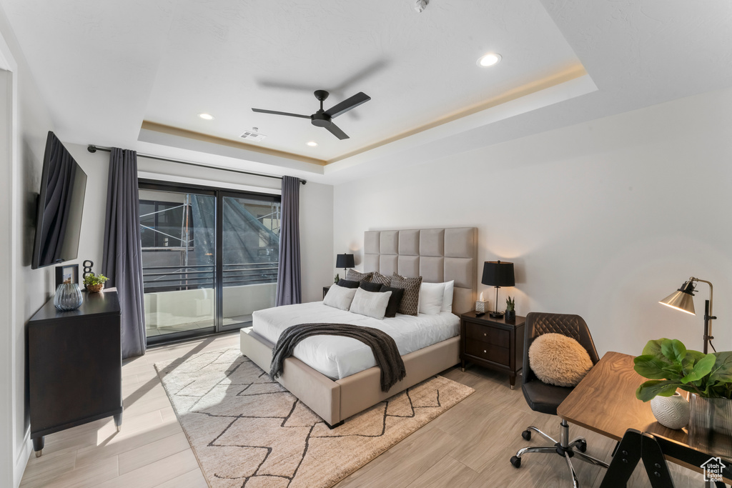 Bedroom featuring a tray ceiling, access to exterior, light wood finished floors, recessed lighting, and a ceiling fan