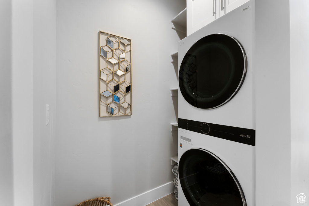 Clothes washing area with stacked washer / drying machine, baseboards, and wood finished floors
