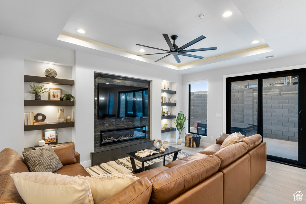 Living area featuring a tile fireplace, a tray ceiling, a ceiling fan, recessed lighting, and light wood-style flooring