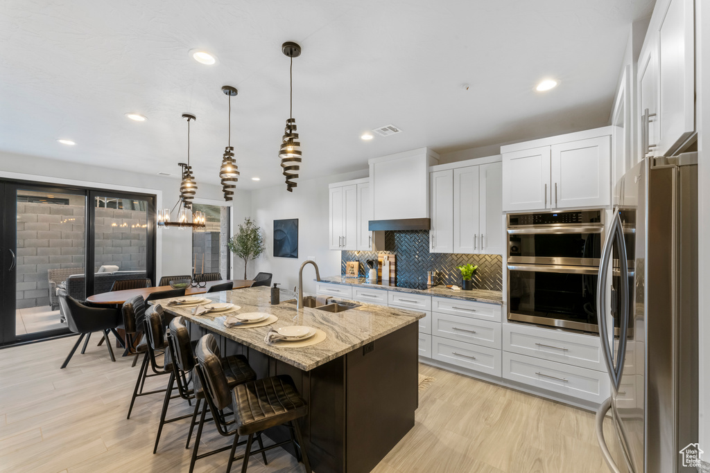 Kitchen with a sink, appliances with stainless steel finishes, light stone counters, decorative backsplash, and white cabinetry