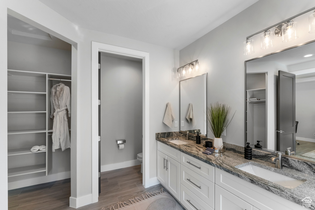 Full bathroom featuring toilet, wood finished floors, double vanity, and baseboards