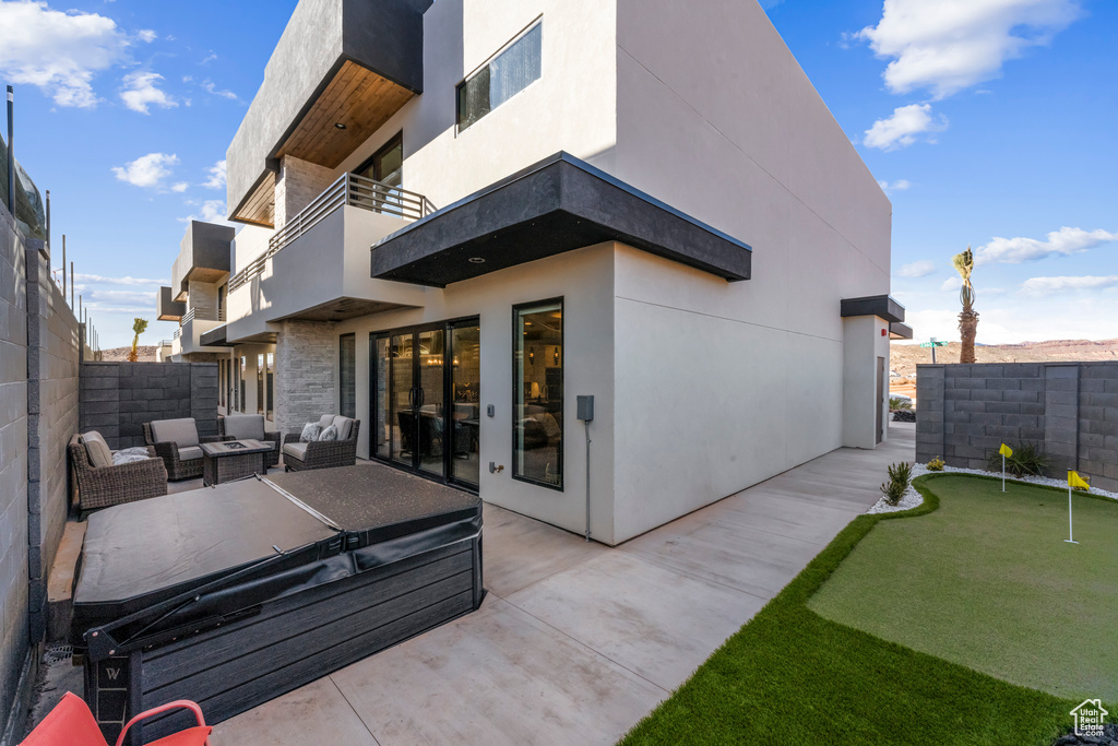 Rear view of property featuring an area to practice putting, a patio area, a balcony, a fenced backyard, and an outdoor hangout area