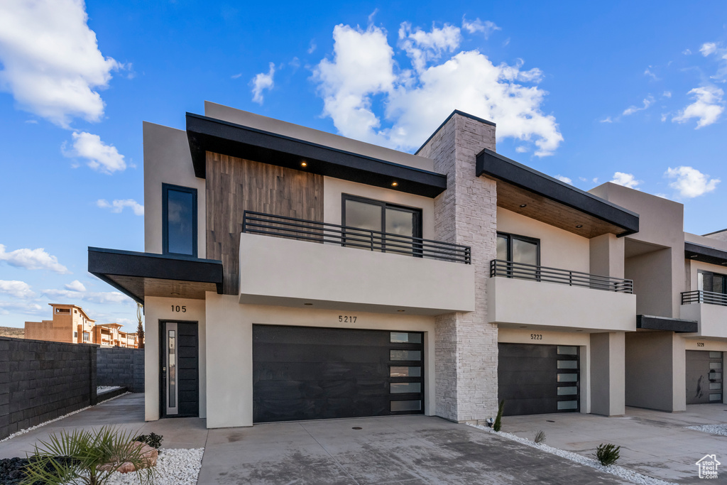 View of front of property featuring an attached garage, driveway, stucco siding, a balcony, and fence