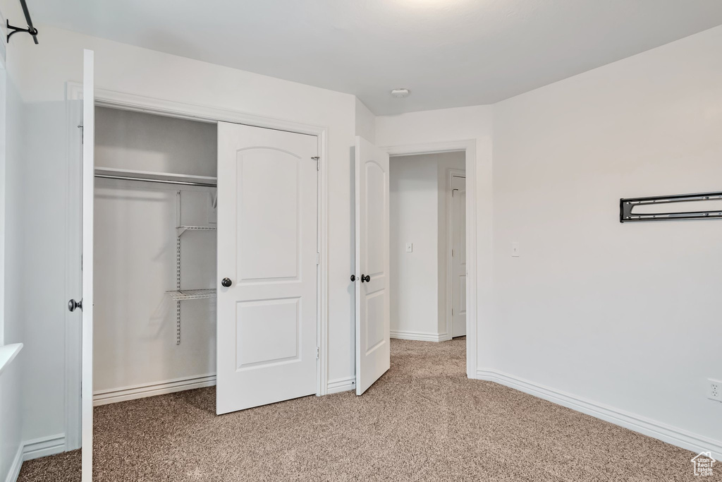 Unfurnished bedroom with light carpet, a closet, and baseboards