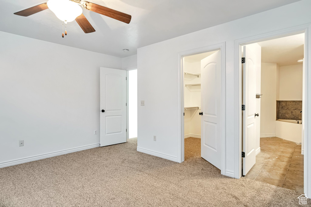 Unfurnished bedroom with light carpet, a spacious closet, baseboards, a closet, and a ceiling fan