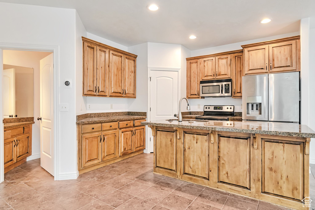 Kitchen featuring stainless steel appliances, a sink, a kitchen island with sink, recessed lighting, and light stone counters