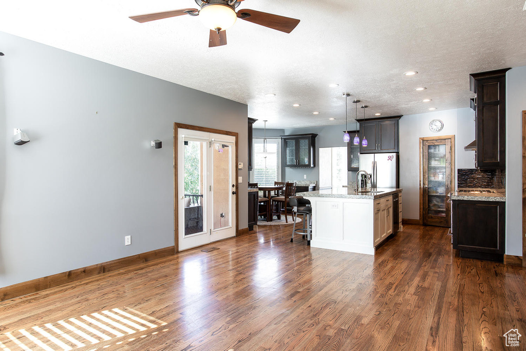 Kitchen with stainless steel refrigerator with ice dispenser, an island with sink, dark wood finished floors, a breakfast bar, and a ceiling fan