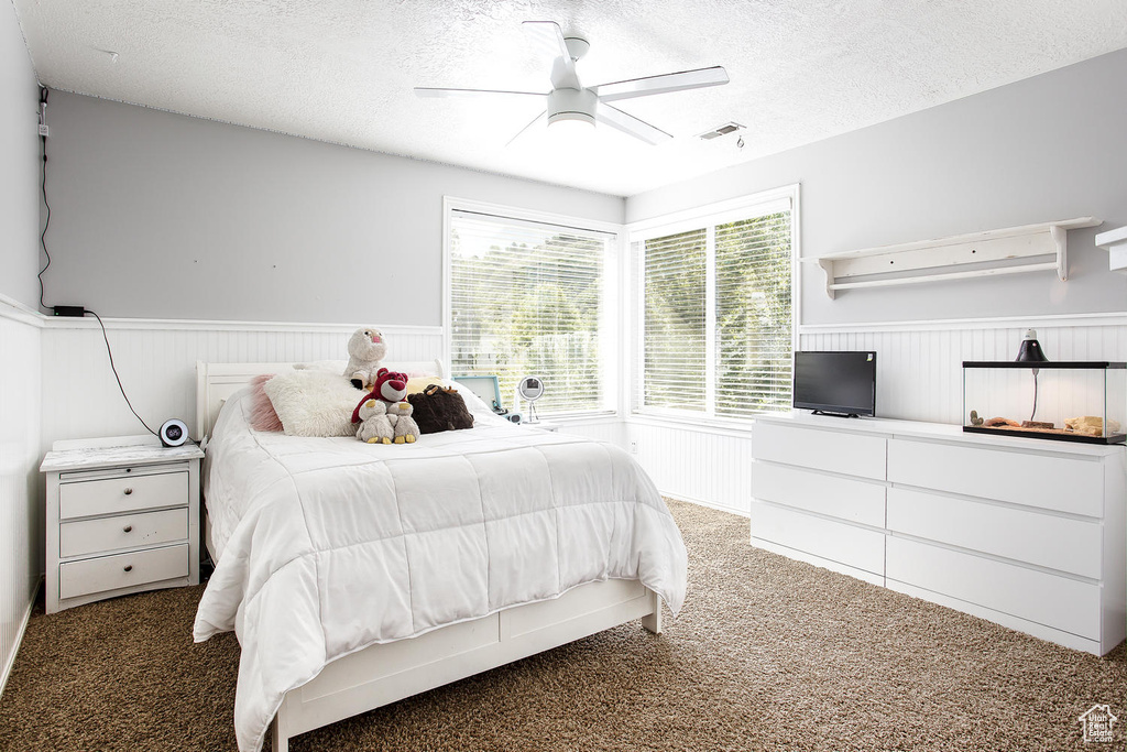 Bedroom with a wainscoted wall, carpet flooring, a textured ceiling, and a ceiling fan