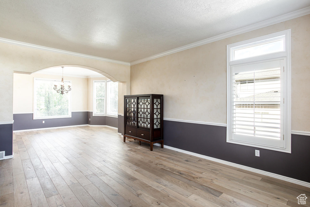 Spare room with a chandelier, hardwood / wood-style flooring, crown molding, arched walkways, and baseboards