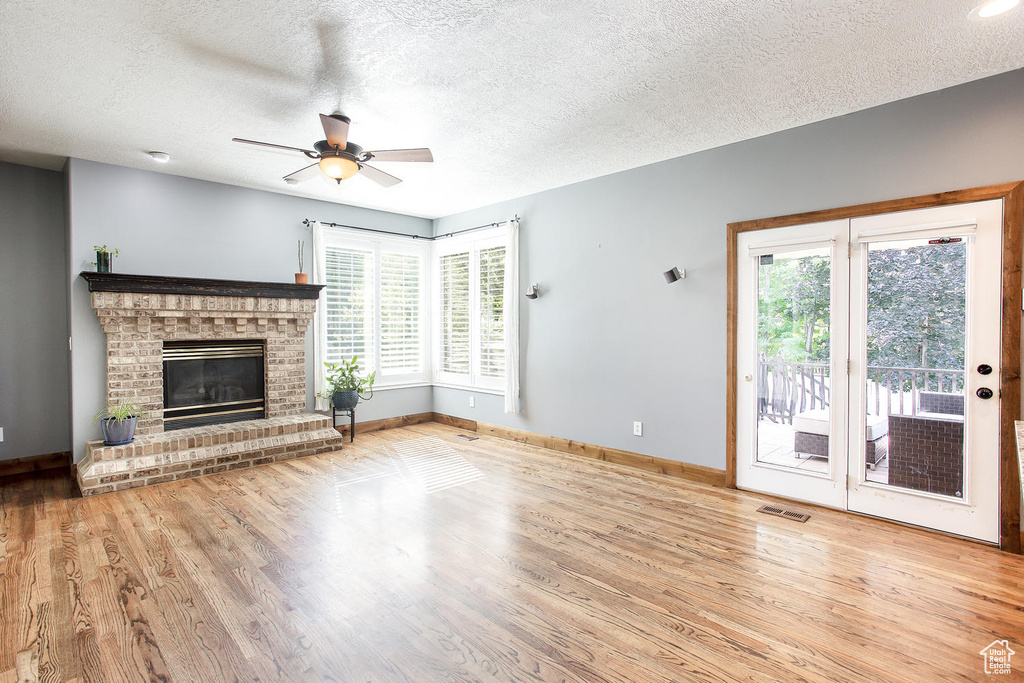Unfurnished living room with ceiling fan, wood finished floors, baseboards, a brick fireplace, and a textured ceiling