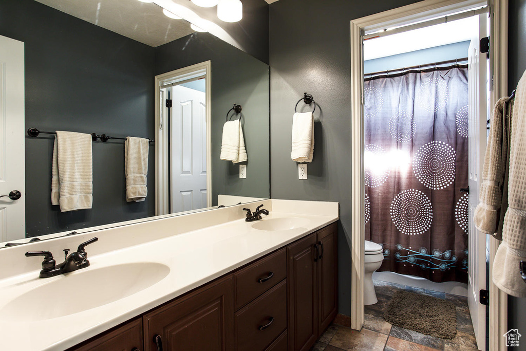 Bathroom featuring toilet, double vanity, and stone finish floors
