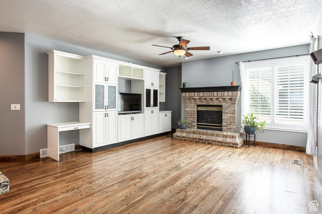 Unfurnished living room featuring a ceiling fan, baseboards, a fireplace, wood finished floors, and a textured ceiling