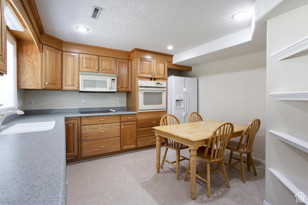 Kitchen with white appliances, a sink, brown cabinets, recessed lighting, and a textured ceiling