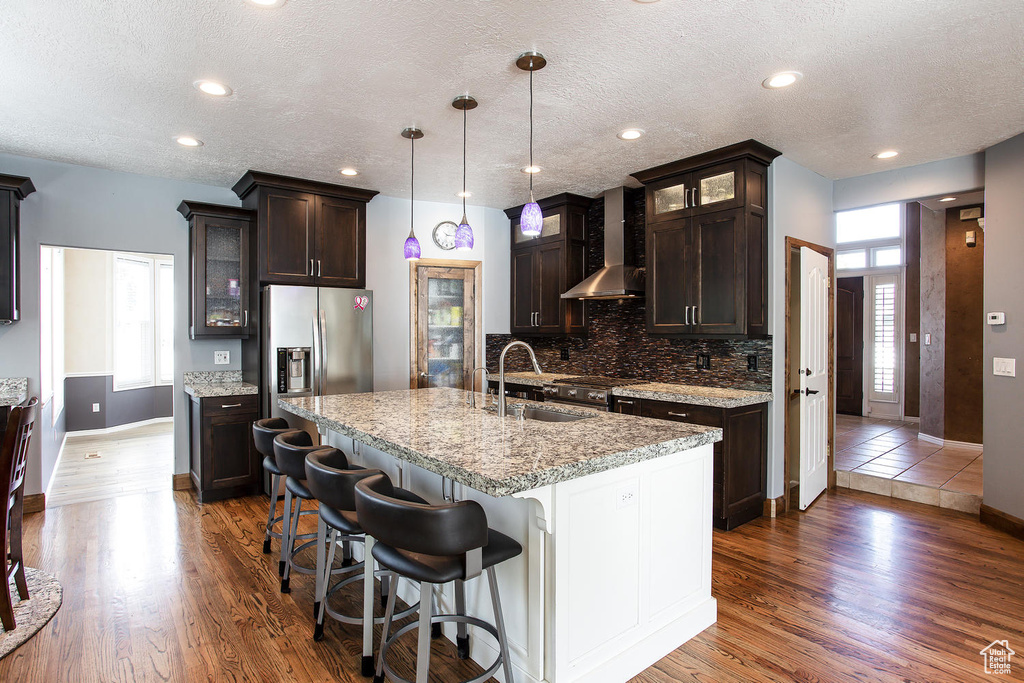 Kitchen featuring wall chimney range hood, a sink, stainless steel appliances, dark brown cabinetry, and baseboards