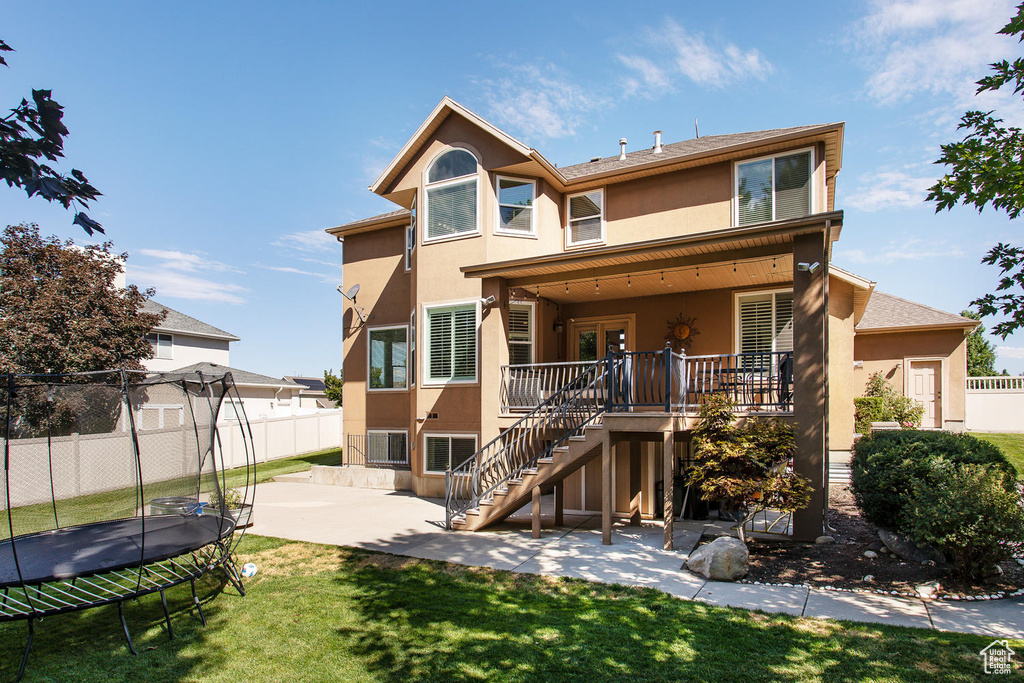 Rear view of house with a trampoline, stucco siding, a patio, stairway, and a deck