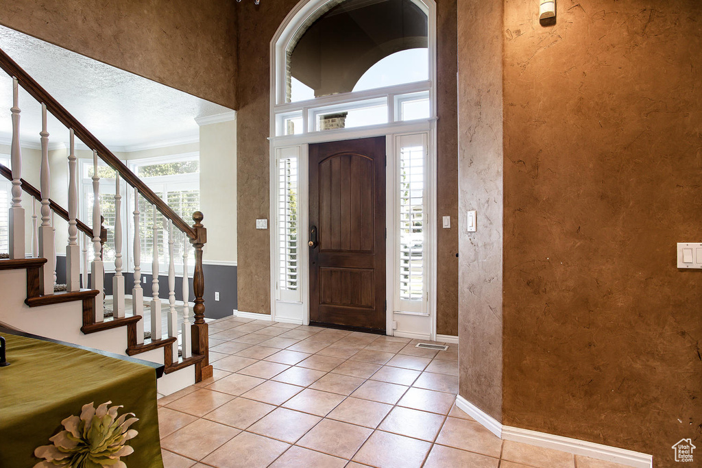 Foyer entrance with baseboards, a textured wall, crown molding, light tile patterned floors, and stairway