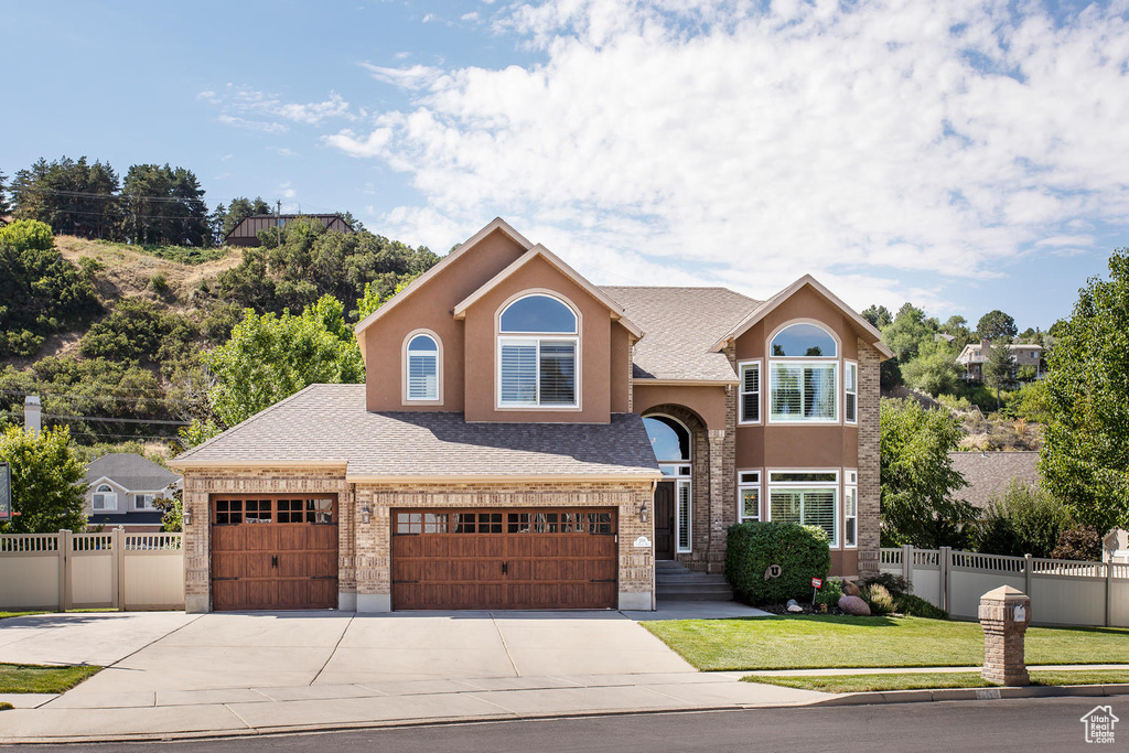 Traditional-style home with driveway, stucco siding, an attached garage, and a shingled roof