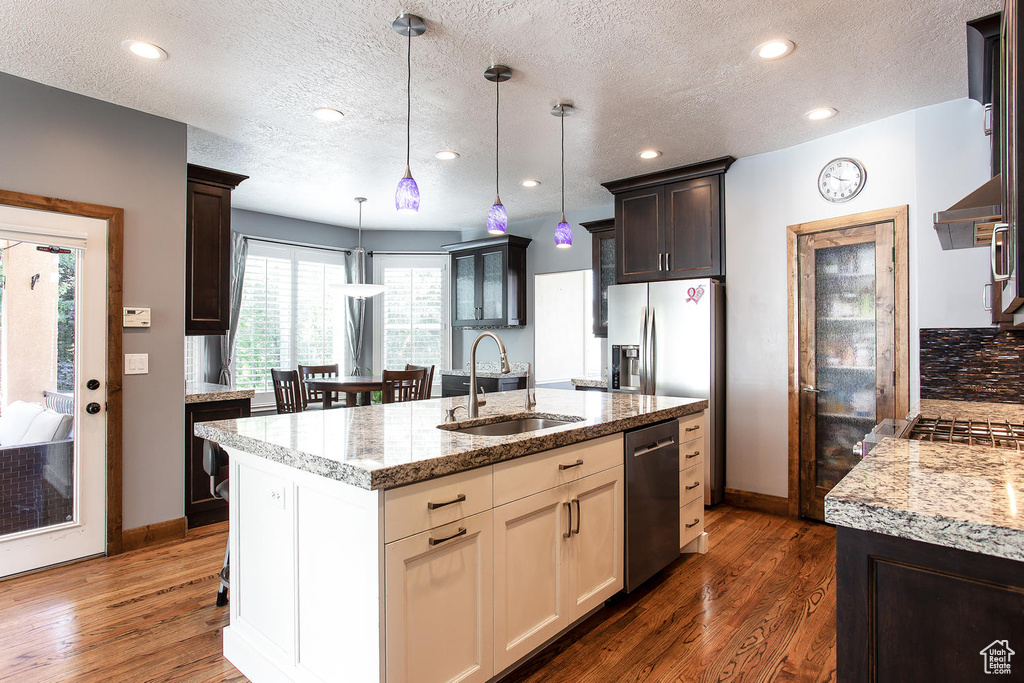 Kitchen featuring a sink, dishwasher, a textured ceiling, light stone countertops, and baseboards