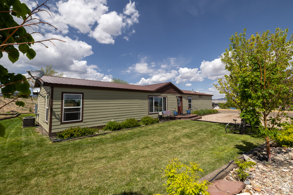 Back of house featuring central AC, a lawn, and metal roof