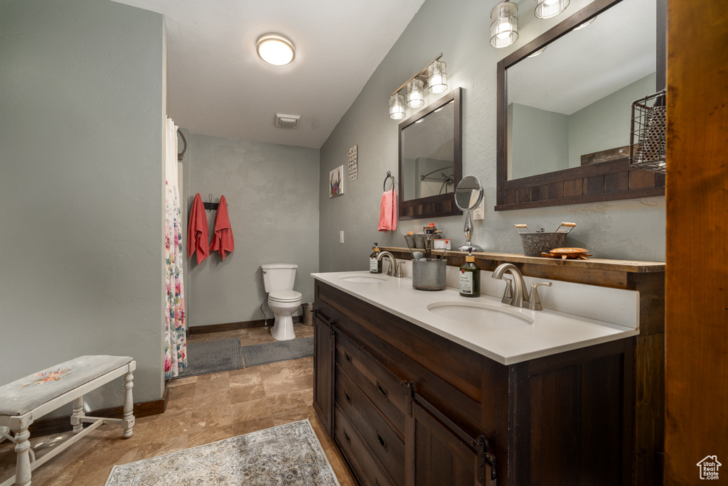 Full bath featuring stone finish floors, toilet, double vanity, and baseboards